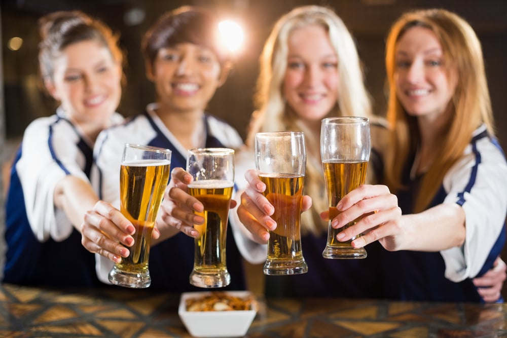 Portrait of smiling friends holding glass of beer in party at bar